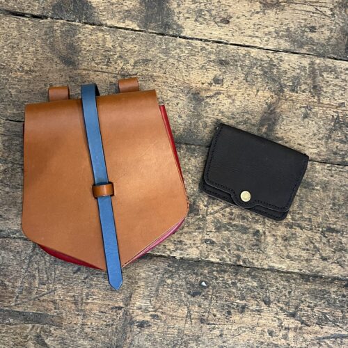 Brown leather belt bag and a black leather card wallet on a wooden floor