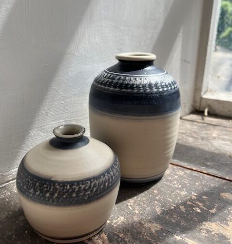 Two cream and blue ceramic vases next to a window.